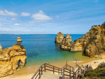 Scalinata in legno verso spiaggia dorata e faraglioni nel mare blu. viaggi di gruppo da torino